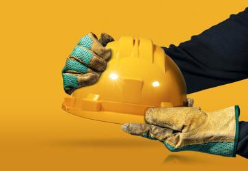 Hands with protective work gloves holding a yellow safety helmet 