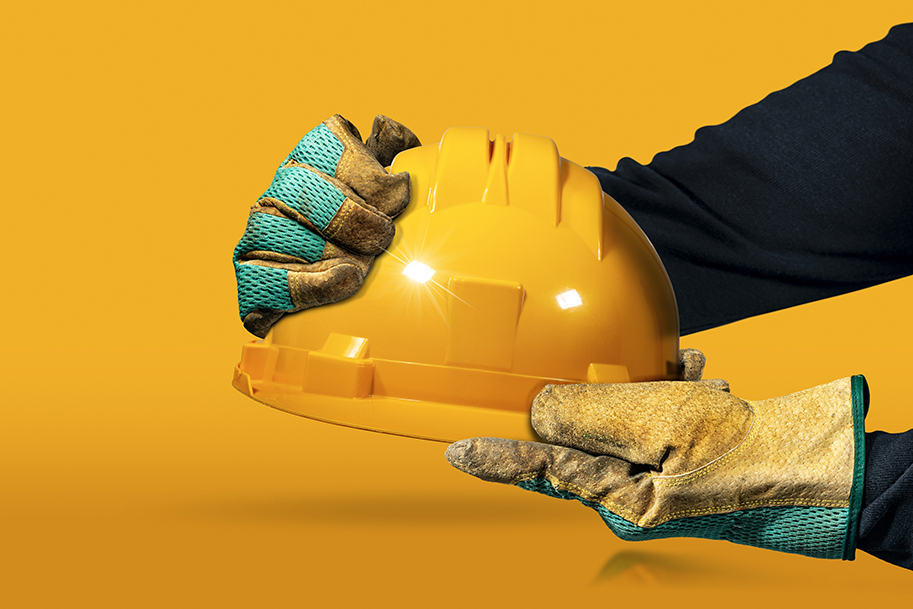 Hands with protective work gloves holding a yellow safety helmet 