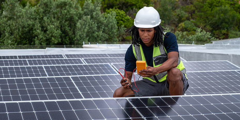 n African man with protective gear checks the voltage of the solar panels that he has just installed on a roof. 