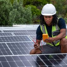 n African man with protective gear checks the voltage of the solar panels that he has just installed on a roof. 