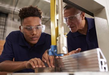 Carpenter Training Male Apprentice To Use Mechanized Saw