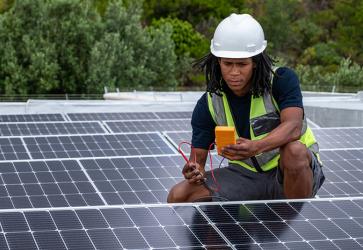 n African man with protective gear checks the voltage of the solar panels that he has just installed on a roof. 